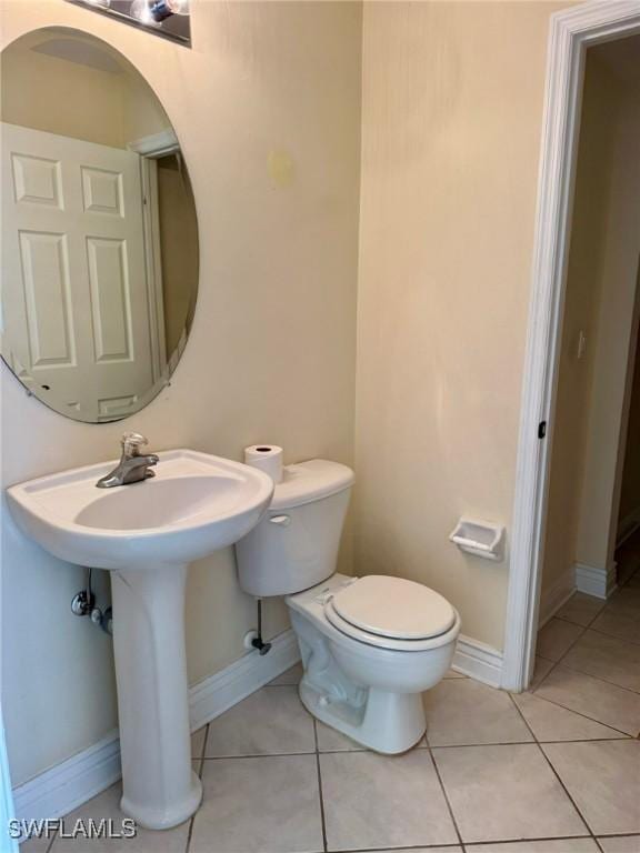 half bathroom with tile patterned flooring, toilet, and baseboards