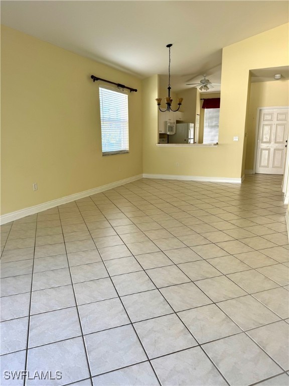 unfurnished living room featuring light tile patterned floors, ceiling fan with notable chandelier, and baseboards