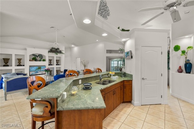 kitchen featuring light tile patterned floors, brown cabinetry, a sink, and a ceiling fan