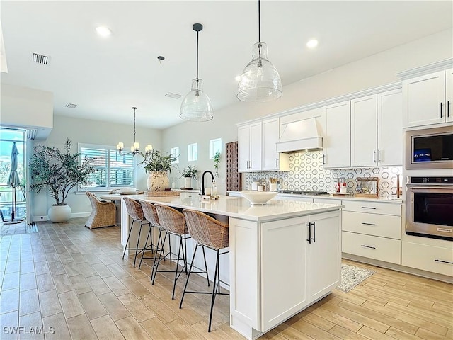 7041 Del Webb Oak Creek Blvd, North Fort Myers, FL 33917 - kitchen featuring tasteful backsplash, visible vents, white cabinets, custom range hood, and appliances with stainless steel finishes