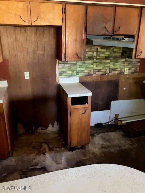 kitchen featuring under cabinet range hood, brown cabinets, tasteful backsplash, and light countertops