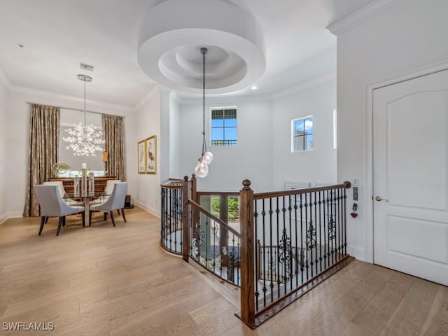 corridor with visible vents, light wood-style flooring, ornamental molding, a raised ceiling, and an upstairs landing