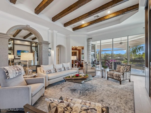 living room featuring beamed ceiling, visible vents, hardwood / wood-style flooring, arched walkways, and a high ceiling