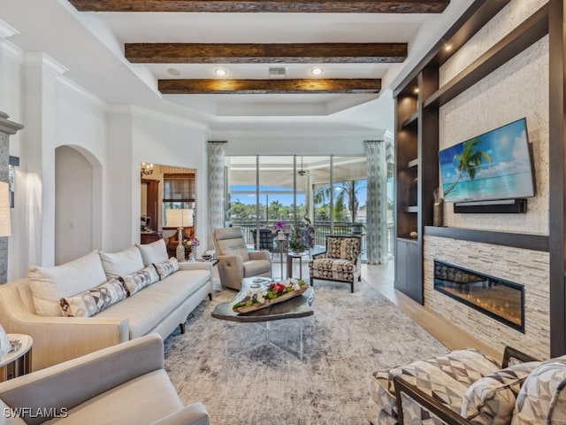 living room with wood finished floors, arched walkways, a sunroom, a stone fireplace, and beamed ceiling