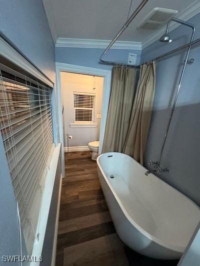 bathroom with baseboards, toilet, a soaking tub, wood finished floors, and crown molding