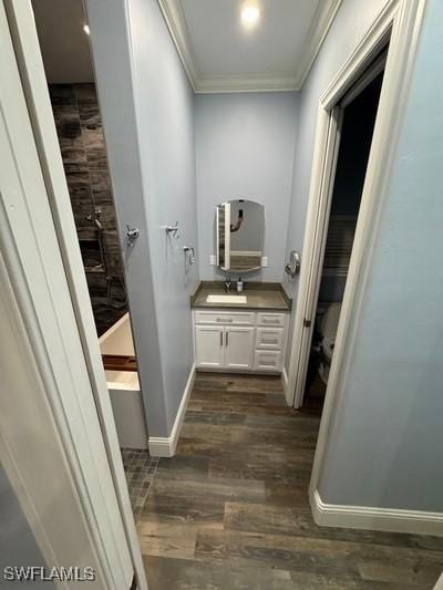 bathroom with a tub to relax in, ornamental molding, vanity, wood finished floors, and baseboards