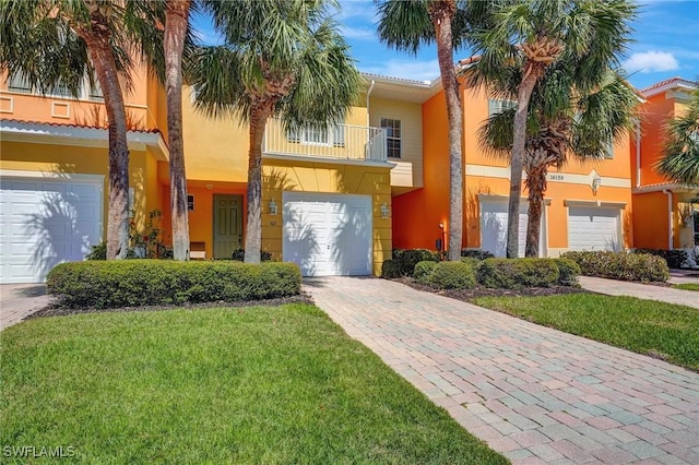 view of front of property with stucco siding, driveway, a front yard, an attached garage, and a balcony