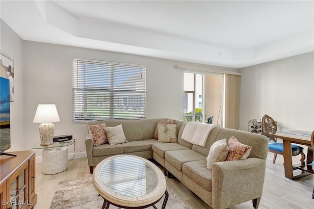 living area featuring a wealth of natural light, light wood-style flooring, a raised ceiling, and baseboards