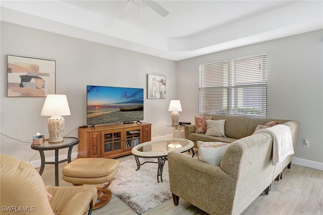 living room with light wood finished floors, a ceiling fan, a tray ceiling, and baseboards