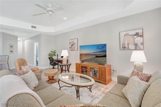 living area with wood finished floors, visible vents, baseboards, ceiling fan, and a raised ceiling