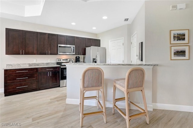 kitchen with light wood finished floors, dark brown cabinets, stainless steel appliances, and a kitchen bar