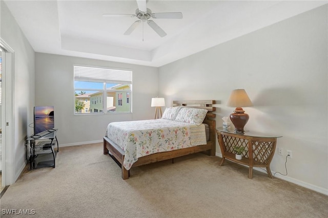 bedroom with light colored carpet, baseboards, a tray ceiling, and a ceiling fan