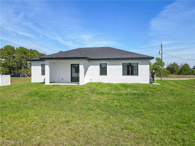 back of property featuring roof with shingles, a lawn, and stucco siding