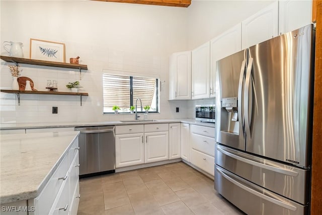 kitchen featuring appliances with stainless steel finishes, a sink, tasteful backsplash, light tile patterned floors, and white cabinetry