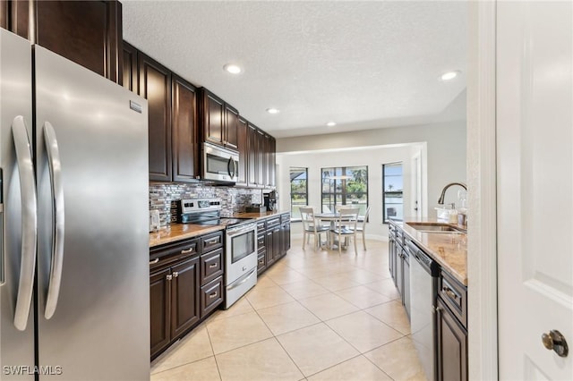 kitchen featuring a sink, backsplash, stainless steel appliances, light tile patterned floors, and dark brown cabinets