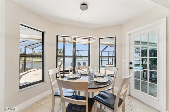 dining room with light tile patterned floors, a water view, baseboards, and a sunroom