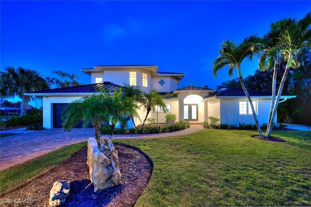 view of front of property with decorative driveway, stucco siding, a front yard, a standing seam roof, and metal roof