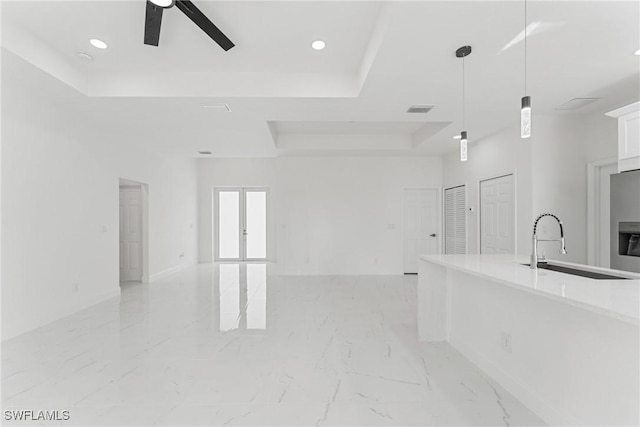 interior space featuring white cabinets, marble finish floor, a raised ceiling, and open floor plan