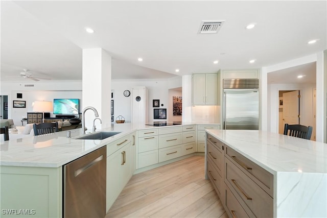 kitchen with visible vents, light stone countertops, appliances with stainless steel finishes, a large island, and a sink