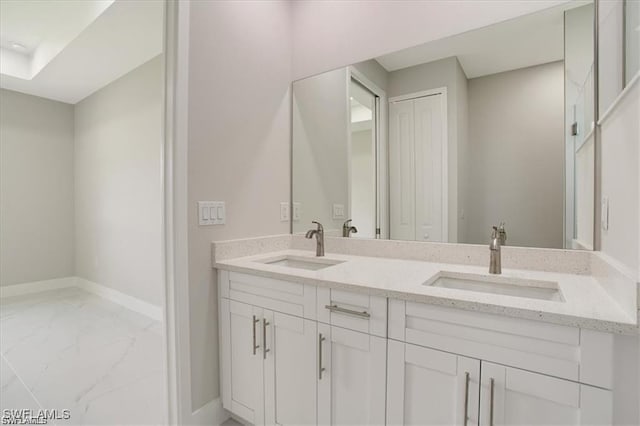 full bath with double vanity, marble finish floor, baseboards, and a sink