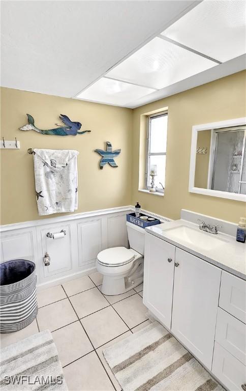 bathroom with vanity, a wainscoted wall, tile patterned flooring, a decorative wall, and toilet