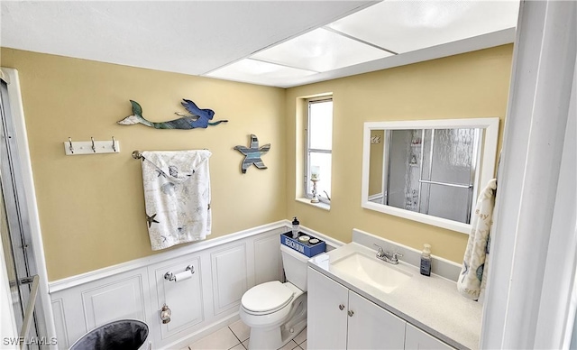 bathroom featuring vanity, tile patterned flooring, wainscoting, a decorative wall, and toilet