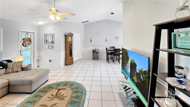 living area featuring a ceiling fan, a wainscoted wall, visible vents, light tile patterned flooring, and vaulted ceiling