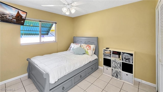 bedroom featuring light tile patterned floors, ceiling fan, a textured ceiling, and baseboards