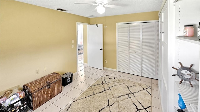 interior space featuring light tile patterned floors, a ceiling fan, visible vents, a closet, and a textured ceiling