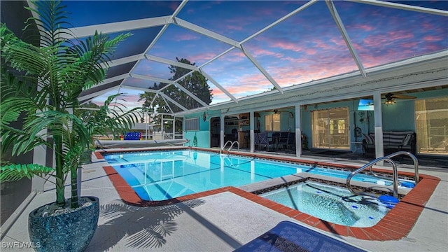 pool at dusk featuring a patio, a lanai, a ceiling fan, and a pool with connected hot tub