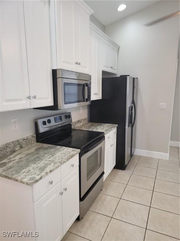 kitchen featuring light tile patterned floors, appliances with stainless steel finishes, baseboards, and white cabinets