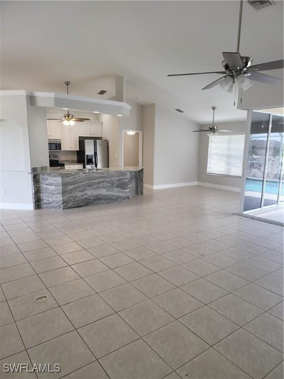 unfurnished living room with light tile patterned floors, visible vents, a ceiling fan, and baseboards