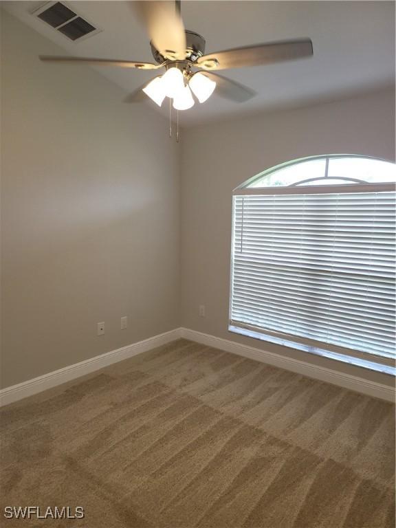 carpeted empty room featuring a ceiling fan, visible vents, and baseboards