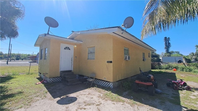 view of home's exterior with stucco siding, entry steps, crawl space, fence, and cooling unit