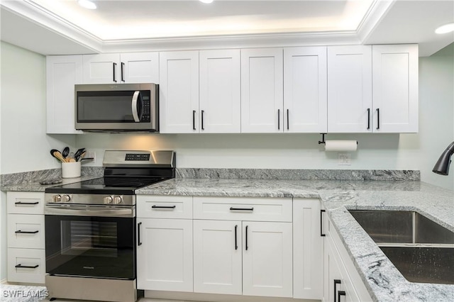 kitchen with light stone counters, crown molding, stainless steel appliances, white cabinets, and a sink