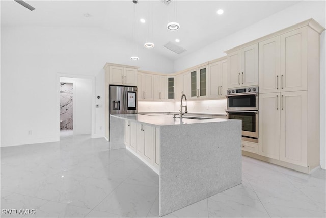 kitchen featuring marble finish floor, cream cabinetry, a center island with sink, appliances with stainless steel finishes, and a sink