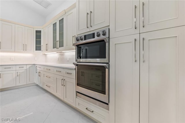 kitchen featuring marble finish floor, tasteful backsplash, light countertops, stainless steel double oven, and vaulted ceiling