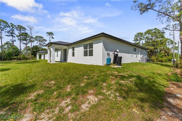 back of house featuring a lawn, central AC unit, and stucco siding