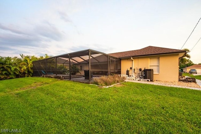 rear view of house with glass enclosure, a lawn, and stucco siding