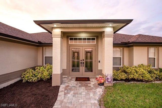 entrance to property featuring french doors, roof with shingles, and stucco siding