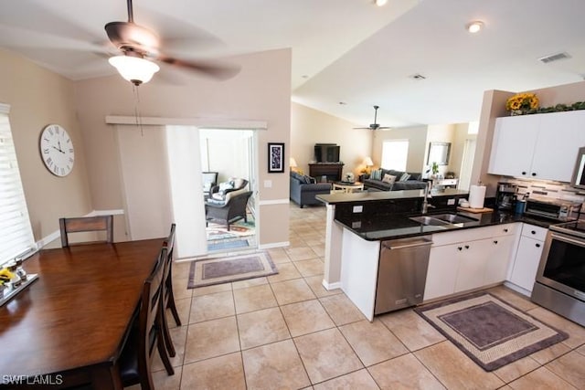 kitchen with light tile patterned floors, dark countertops, appliances with stainless steel finishes, a sink, and a peninsula