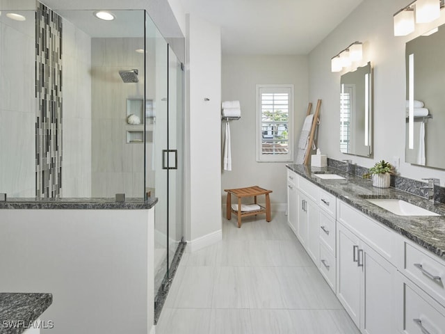 bathroom featuring double vanity, a stall shower, a sink, and baseboards