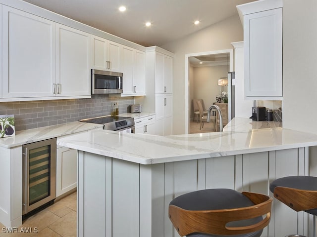 kitchen featuring beverage cooler, a peninsula, white cabinetry, appliances with stainless steel finishes, and tasteful backsplash