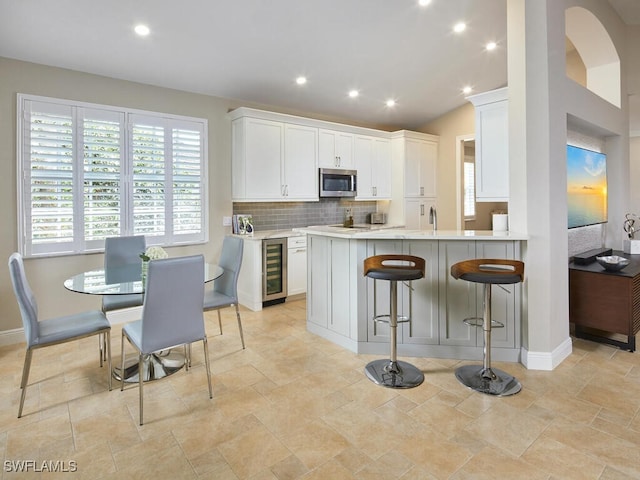 kitchen featuring tasteful backsplash, light countertops, stainless steel microwave, white cabinets, and beverage cooler