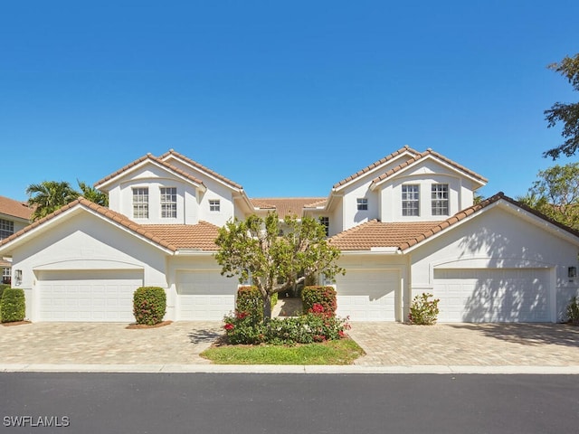 mediterranean / spanish house with a garage, decorative driveway, a tile roof, and stucco siding