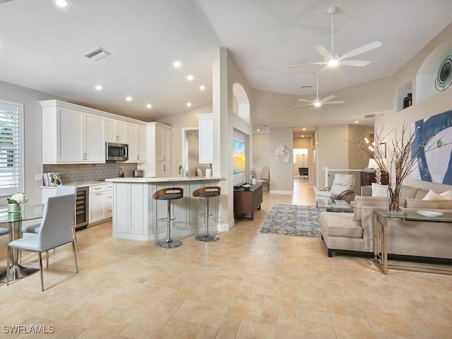 kitchen with wine cooler, a breakfast bar, white cabinetry, open floor plan, and stainless steel microwave