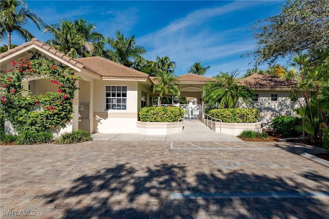 mediterranean / spanish home featuring a tile roof, a gate, and stucco siding