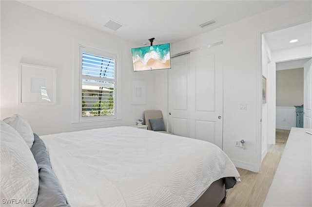 bedroom with light wood-type flooring, baseboards, visible vents, and a closet