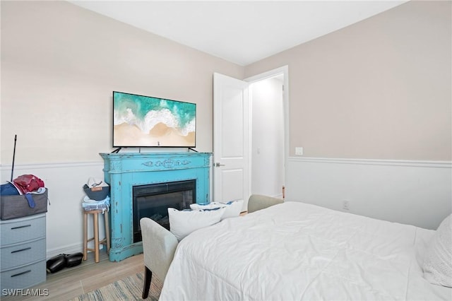 bedroom featuring a glass covered fireplace and wood finished floors