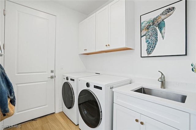 washroom with cabinet space, light wood finished floors, a sink, and independent washer and dryer